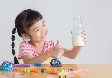 asian girl take a bottle of milk with play dough on the wooden table