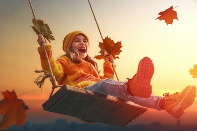 happy child girl on swing in sunset fall. little kid playing in the autumn on the nature walk.