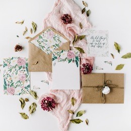 workspace. wedding invitation cards, craft envelopes, pink and red roses and green leaves on white background. overhead view. flat lay, top view
