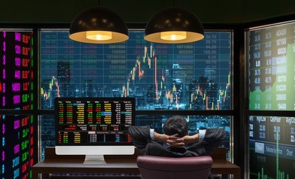 back side of sitting businessman who is looking at big screen and desktop computer showing the trading graph of stock market exchange graph background, business trading and finance concept