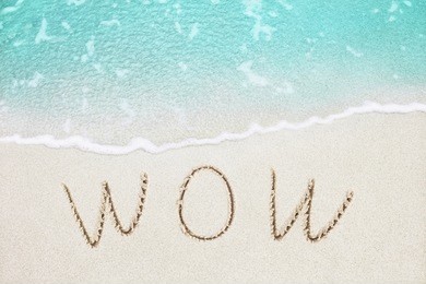 wow handwritten on the sandy beach with beautiful soft azure wave on background
