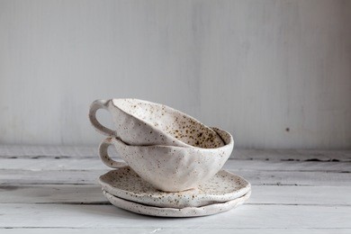 set of white pottery on a white background, white pottery in brown speckled, plates and cups from clay