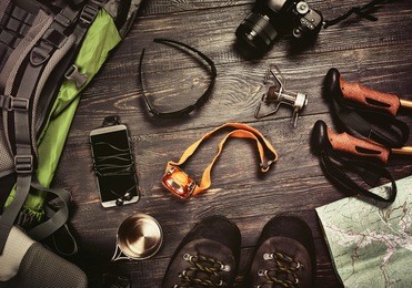 hiking accessories set on dark wooden background:  boots, backpack, sunglasses, photo camera, map, smartphone, flashlight and others. top view. vintage retro effect