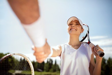 satisfied young female tennis player greets with trainer on tennis court