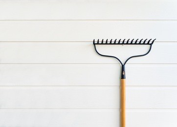 minimalist image of new rake hanging on clean white wooden texture wall with copy space