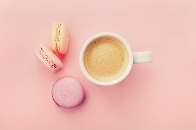 cup of coffee with macaron on pink background from above, flat lay