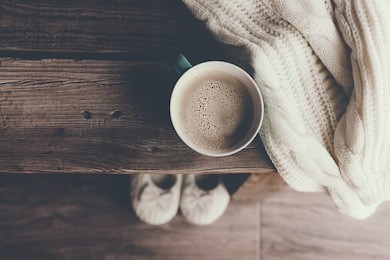 cup of hot coffee on rustic wooden bench, closeup photo of warm sweater with mug and slippers, winter morning concept, top view