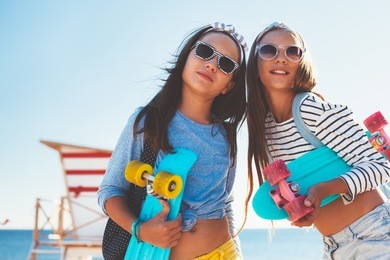 two 10 years old children wearing cool clothing posing with colorful skateboards on the beach, urban style, pre teen summer fashion.