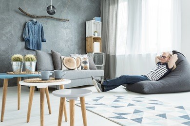 modern minimalistic and bright living room in shades of cyan with sofa, three coffee tables, carpet, stillage made of wooden cases and a man sitting on a bean bag chair