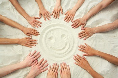 photo of smiling face hands painting on sand surrounded human hands