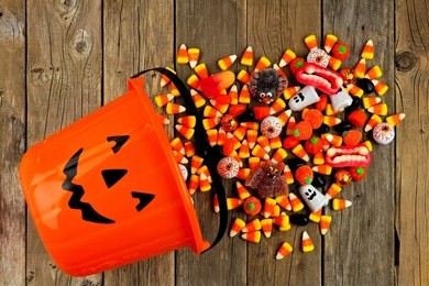 halloween jack o lantern pail with spilling candy, above view on a rustic wood background
