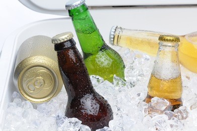 close up of an assortment of beer bottles and cans in cooler with ice horizontal composition