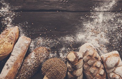 bread border on dark wood with copy space background. brown and white whole grain loaves still life composition with wheat flour sprinkled around. bakery, cooking and grocery store concept.
