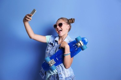 cute young girl taking selfie with skateboard on blue wall background