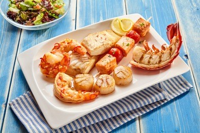 various seafood appetizers consisting of lobster, crab cakes, fish meat and shrimp on plate with striped napkin beside salads
