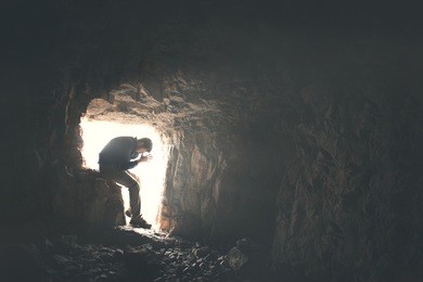sad man praying god in a dark cavern 