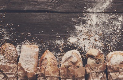 bread border on dark wood with copy space background. brown and white whole grain loaves still life composition with wheat flour sprinkled around. bakery, cooking and grocery store concept.