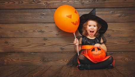 funny child girl in witch costume for halloween with pumpkin jack and orange balloon on a dark wooden background