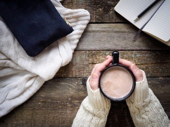 cup of cocoa in hands and office  staff on wooden table