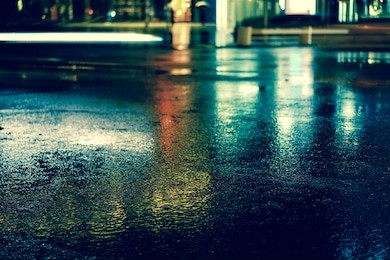 rainstorm in the big city night, light from the shop windows reflected on the road on which cars travel. view from the level of asphalt