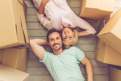 top view of beautiful mature couple in casual clothes looking at camera and smiling while lying on the floor among boxes for move