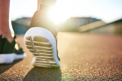 close up low angle view of running shoes with while soles on an empty road as the sun highlights the distance