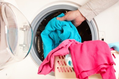 close-up on female hand putting colorful clothes into washing machine drum