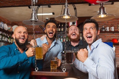 man group in bar screaming and watching football, drinking beer hold mugs, mix race cheerful friends wear shirts meeting pub communicate