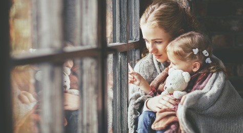 family mother and child daughter keep warm and look out the window on a rainy autumn day