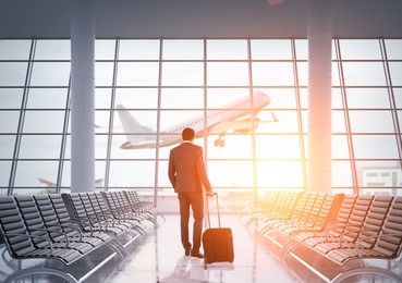 african american businessman in airport waiting area looking at large jet coming off the ground through panoramic window. concept of business trips. toned image