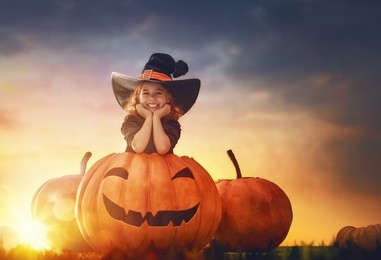 happy halloween! cute little witch with a big pumpkin. beautiful young child girl in witch costume outdoors. 