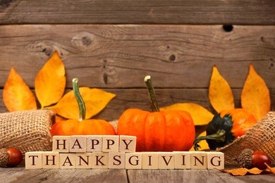 happy thanksgiving wooden blocks against a rustic wood background with pumpkins and autumn leaves