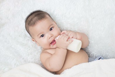baby lying on the white carpet and drinking milk from a bottle.