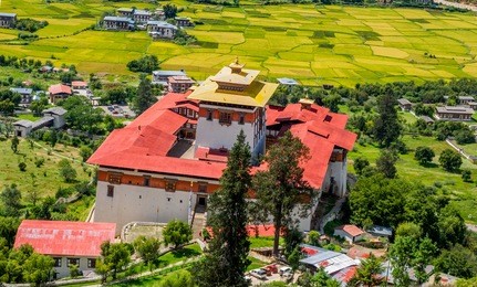 view from above of the rinpung dzong, which is the bhutanese temple over the paro valley with green rice field in a blue background