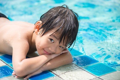 adorable asian child in the pool looks in a camera