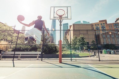 street basketball athlete performing huge slam dunk on the court, new york buildings background