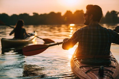 meeting sunset on kayaks. rear view of young couple kayaking on lake together with sunset in the backgrounds