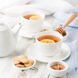 two cups of hot black tea, lemon, homemade cookies and honey on white rustic wooden background. breakfast concept. selective focus