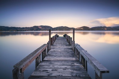wooden pier or jetty on blue lake sunset and sky reflection water. long exposure, versilia massaciuccoli, tuscany, italy.