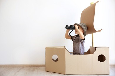 little boy playing with cardboard ship on white wall background