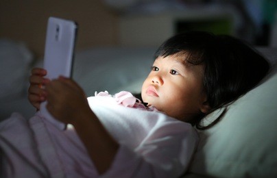 adorable little girl playing smartphone lying on a bed at night