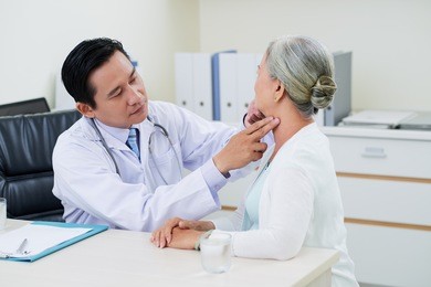 doctor checking thyroid glands of senior woman