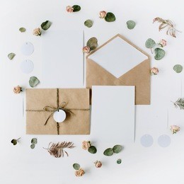 flat lay workspace. wedding invitation cards, craft envelopes, pink and red roses and green leaves on white background. overhead view, top view