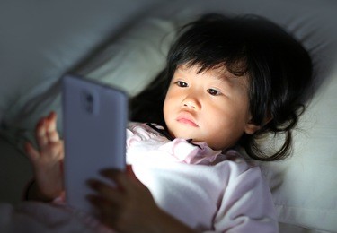 kid girl playing smartphone lying on a bed at night
