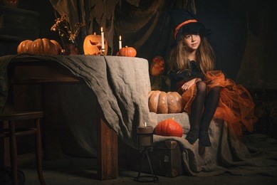 small girl in witch costume sit on the table in halloween decorations