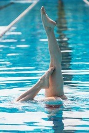 legs detail of professional woman practicing synchronized swimming upside down inside swimming pool.