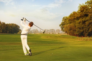 boy golf player hitting by iron from fairway at autumn evening
