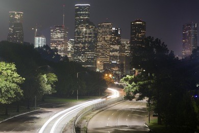 long-exposure of cars racing over a freeway in downtown houston, texas with the houston skyline in the background at night