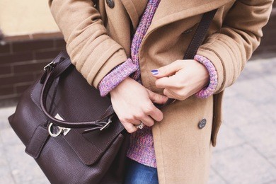 female hands holding a brown leather bag.