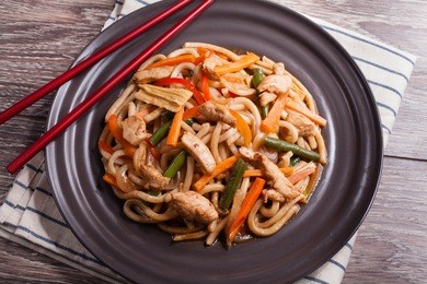 noodles with chicken and vegetables on a dark plate and a linen towel on the wooden background
